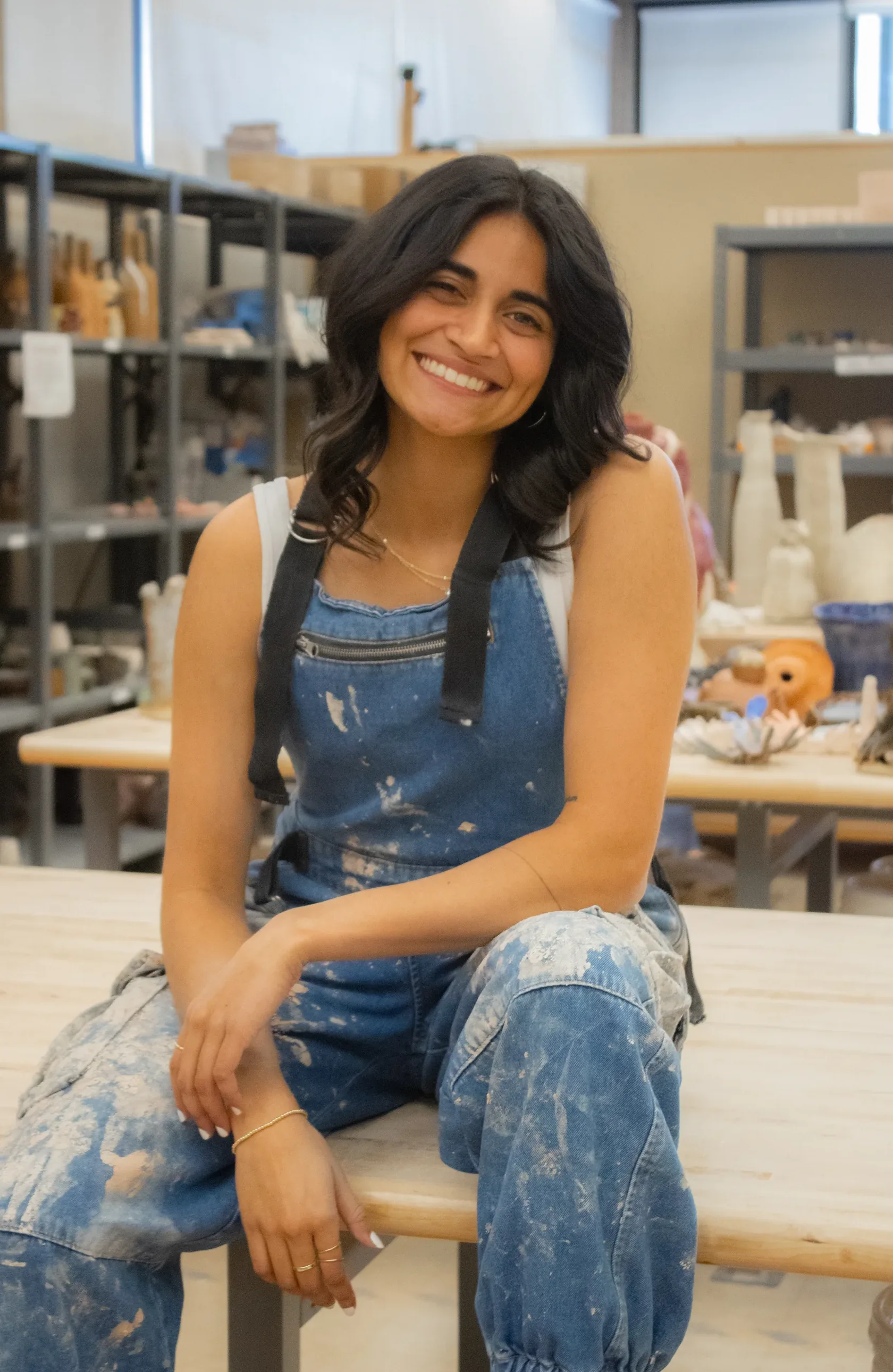 Portrait of Elizabeth Fernandes sitting on a workbench in a ceramics studio
